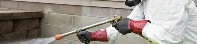 Pest control technician applying exterior insect treatment along a home foundation in New Haven, CT