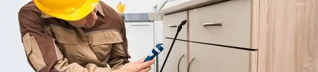Roach exterminator applying treatment under kitchen cabinets in New Haven, CT