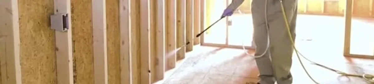 Termite treatment technician applying spray along framing and unfinished walls in New Haven, CT